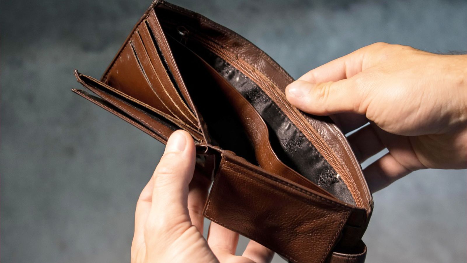 A person opening an empty, brown wallet