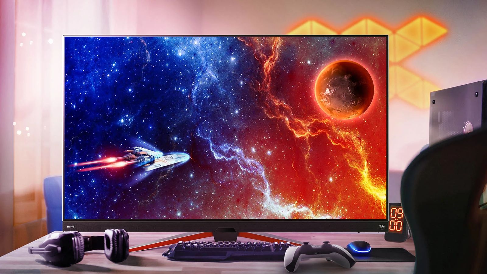 A black OLED monitor with a space scene on the display sat on a desk with a keyboard, headset, controller. and mouse.