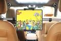 A tablet with Simpsons on the display mounted between two brown leather car seats.