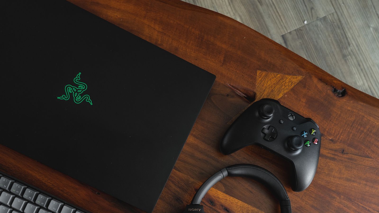 Black Razer gaming laptop on a wood table next to a black Xbox controller.