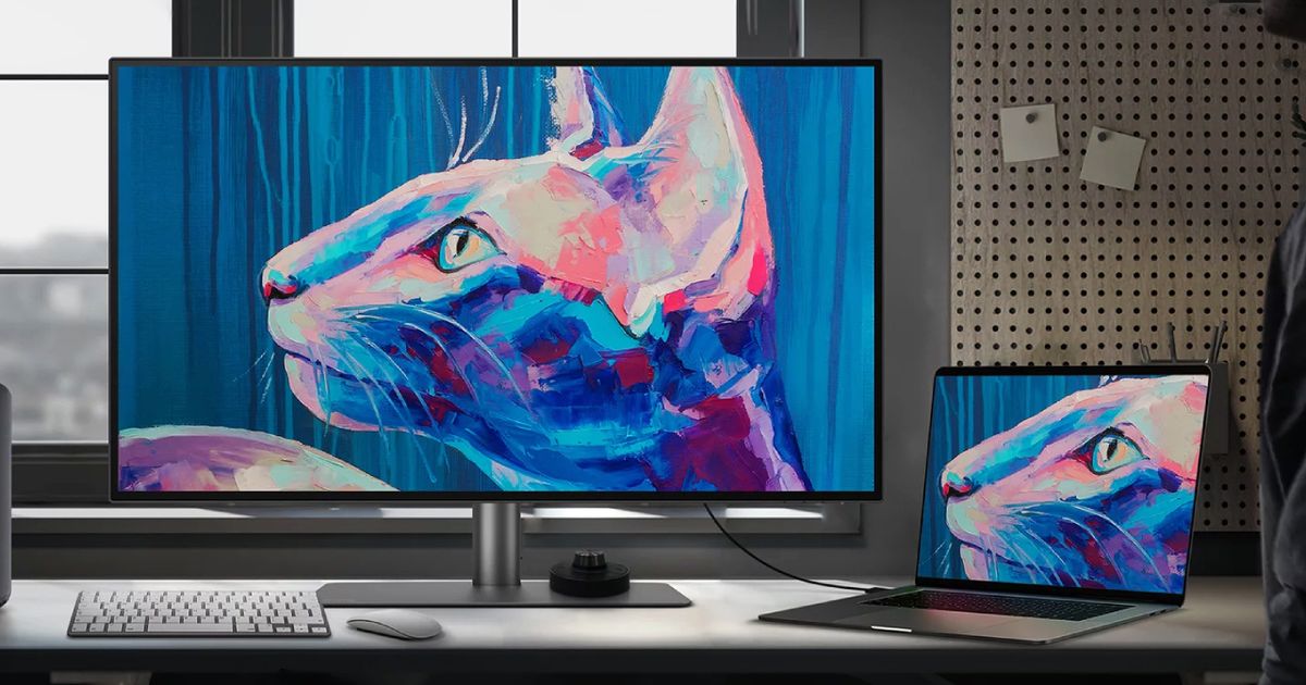 A large monitor with a cat painted in pink, blue, and purple on the display next to a thin laptop with the same image on it.