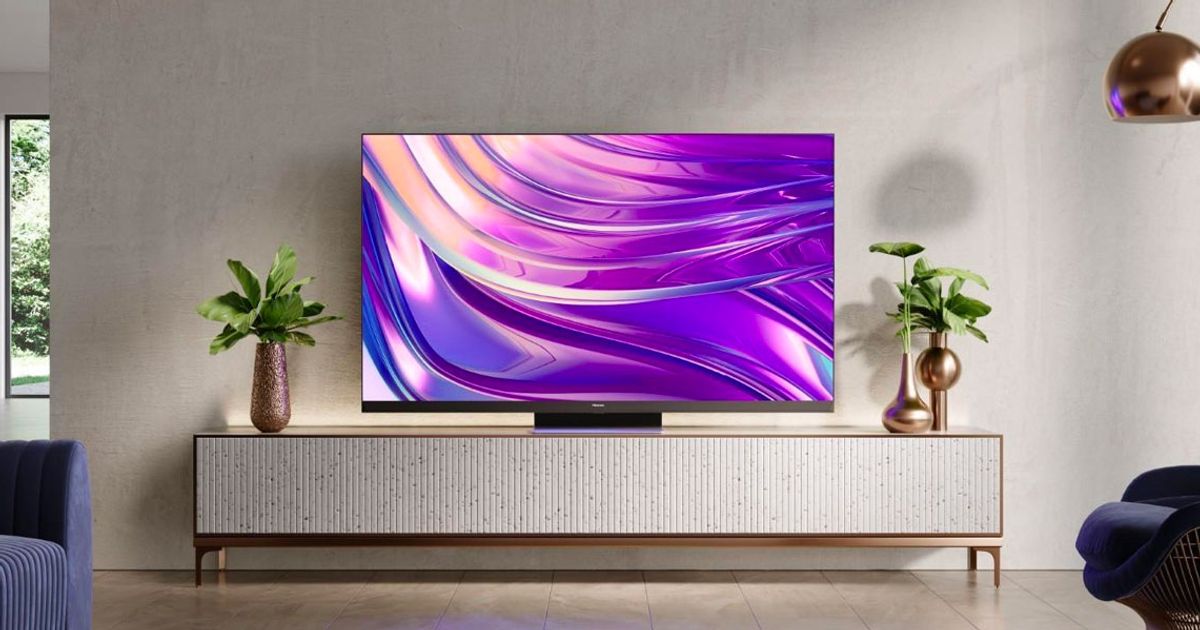 Image of a TV placed on a grey and gold stand between two plants featuring a purple pattern on the display.