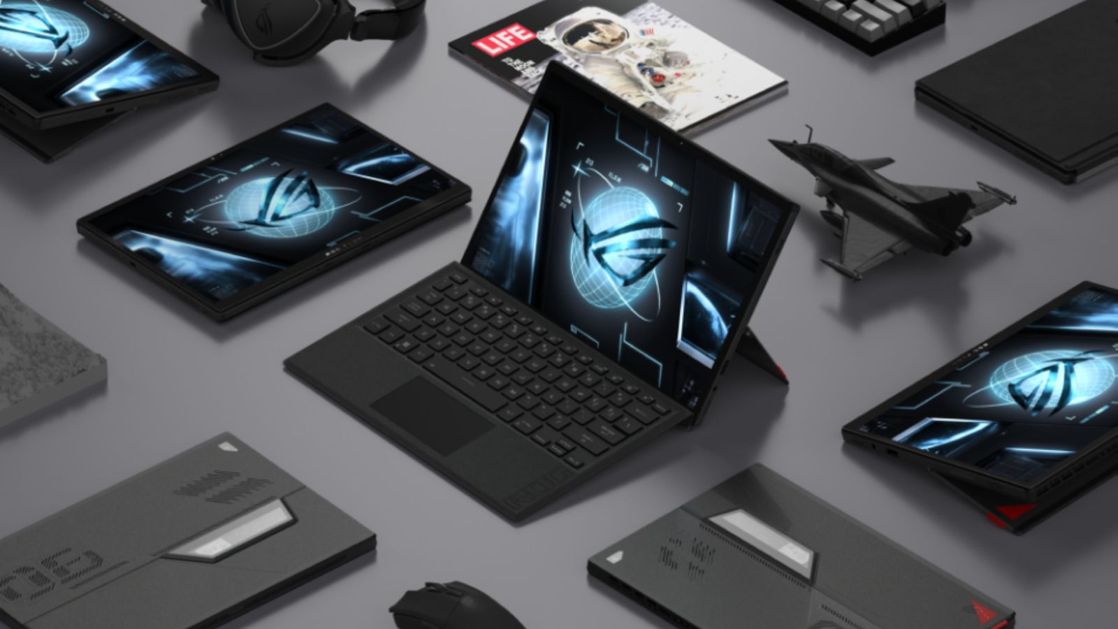ASUS ROG Flow Z13 product image of the laptop propped up in the centre surrounded by other laptops folded into tablets, a magazine, and a small black jet model.