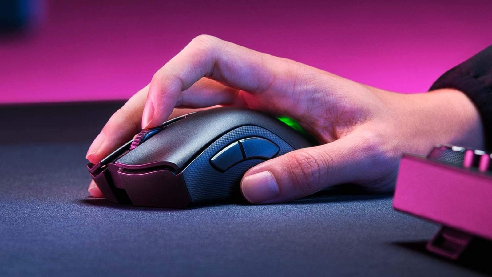 Someone with their hand on a black wireless gaming mouse featuring green lighting on top.