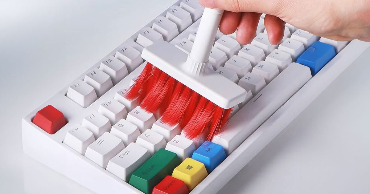 A white keyboard with multiple coloured keys being cleaned by someone holding a white and red brush.