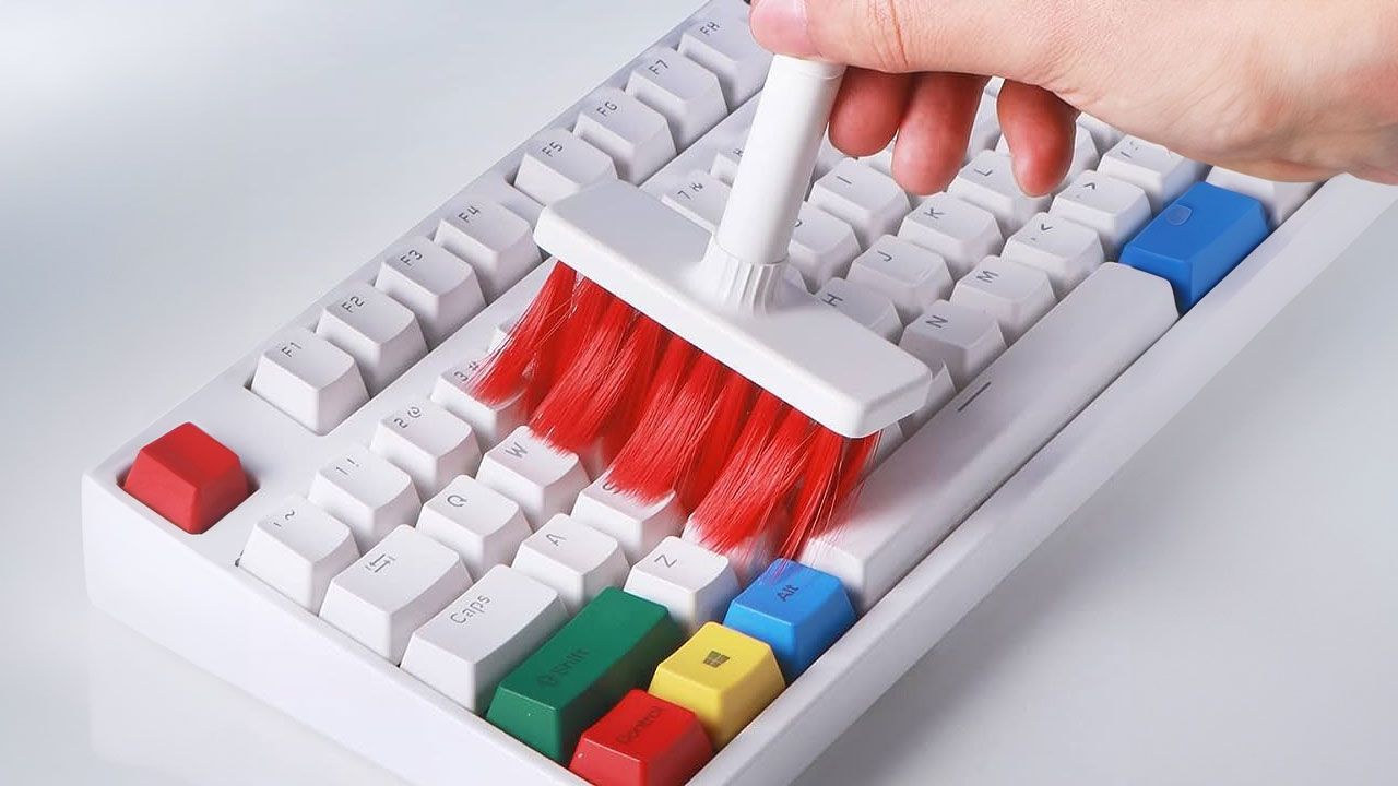 A white keyboard with multiple coloured keys being cleaned by someone holding a white and red brush.