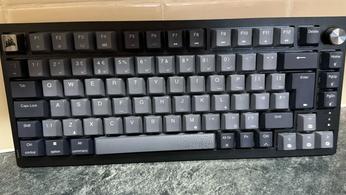 The Corsair K65 Plus Wireless keyboard in front of a tiled wall