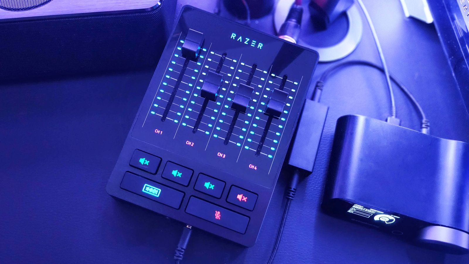 A black audio mixer bathed in blue light, featuring light blue and red lights on it.