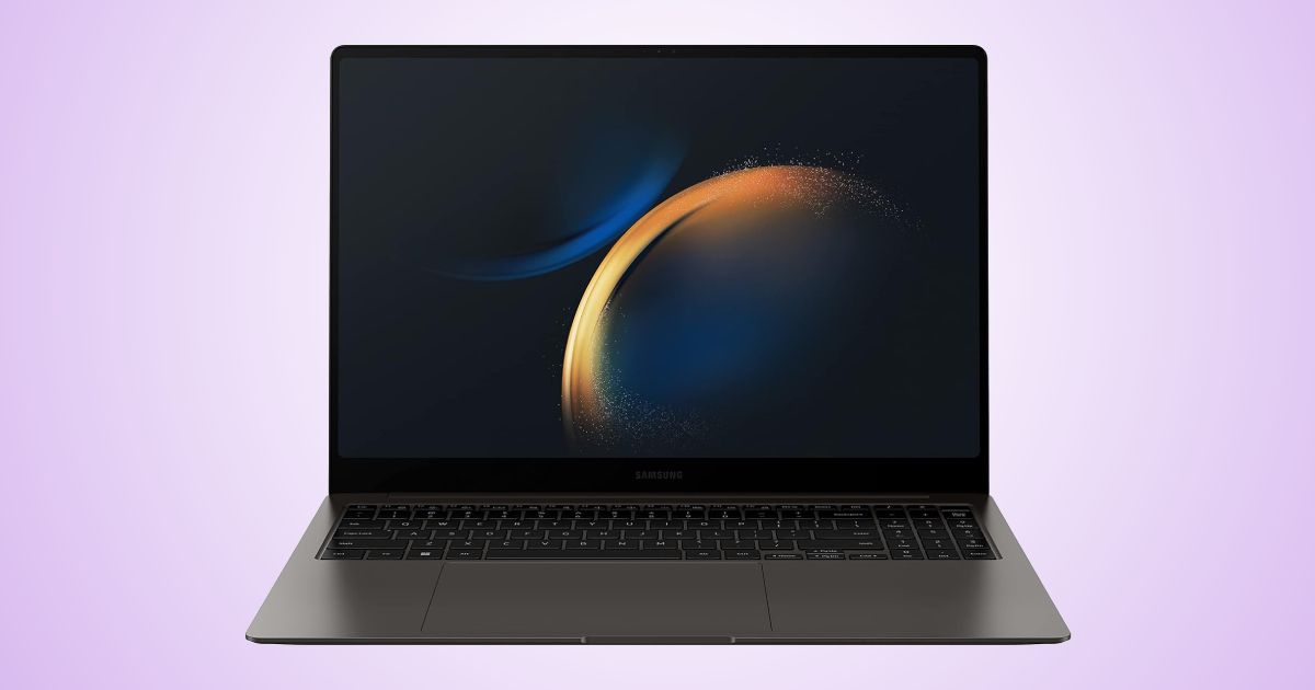 A dark grey and black thin laptop with a dark blue and orange circular pattern on the display in front of a light purple gradient background.