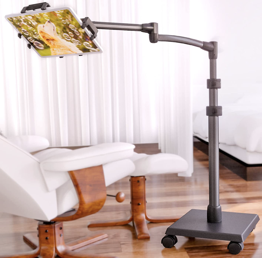 An extendable black stand with a tablet attached over a bed.