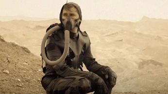a man wearing a gas mask is sitting on the ground in the desert .