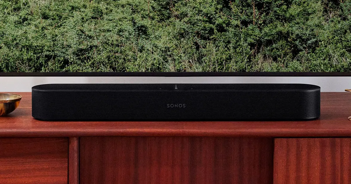 Image of a black soundbar on a brown wooden TV stand in front of a television.