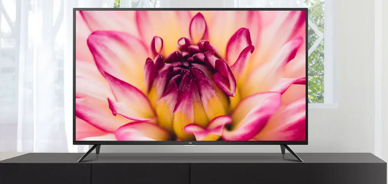 A black TV featuring a pink, white, and yellow flower is placed on top of a black cabinet.