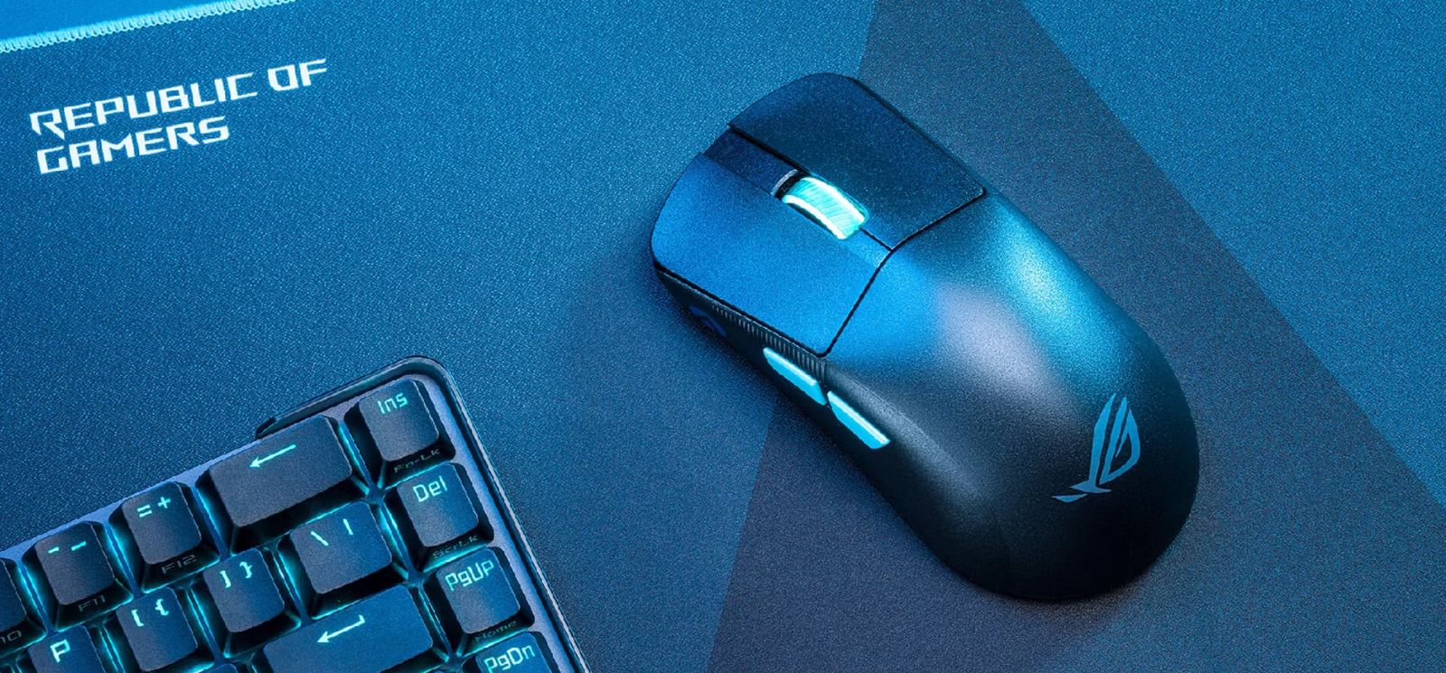 Image of a black wireless mouse with a grey scroll wheel on a Republic of Gamers mat and next to a keyboard in a blue lit room.