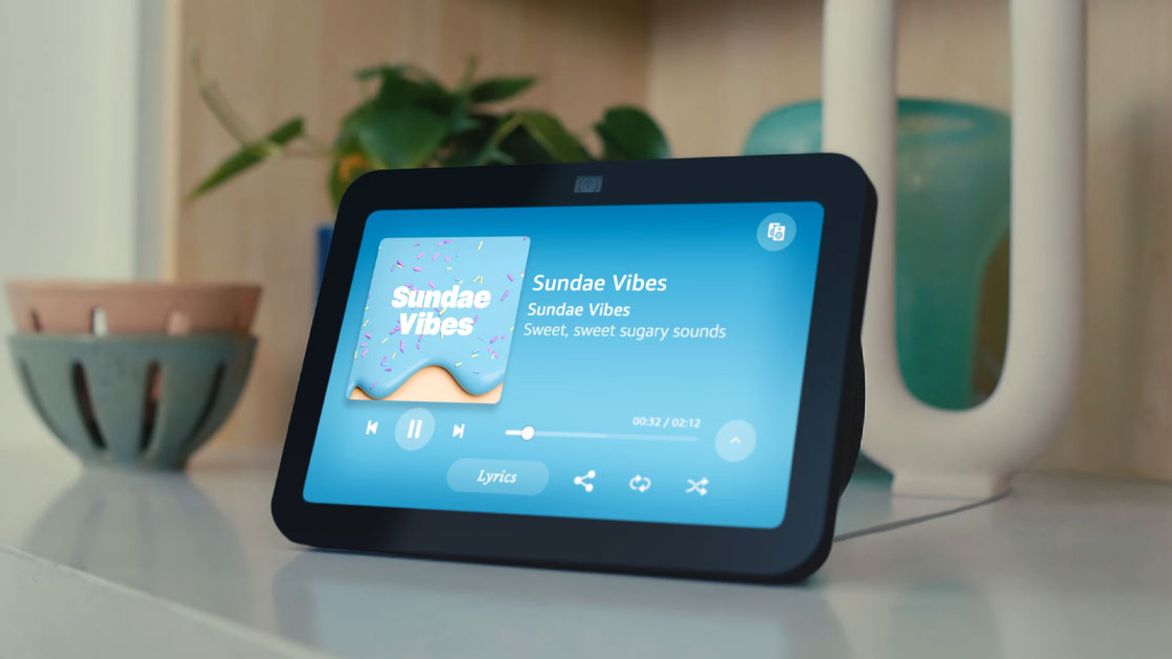 A black Amazon Echo 8 on a wide table top with "Sunset Vibes" song playing on the display.