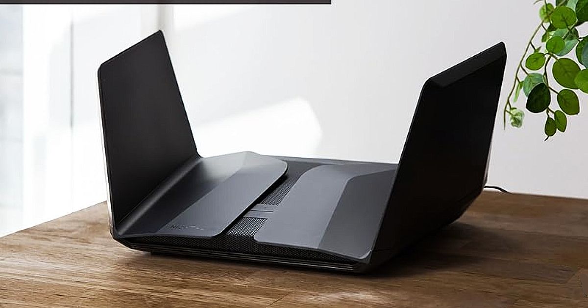 A black WiFi router sat on a brown wooden desk with two winged antennae on either side.