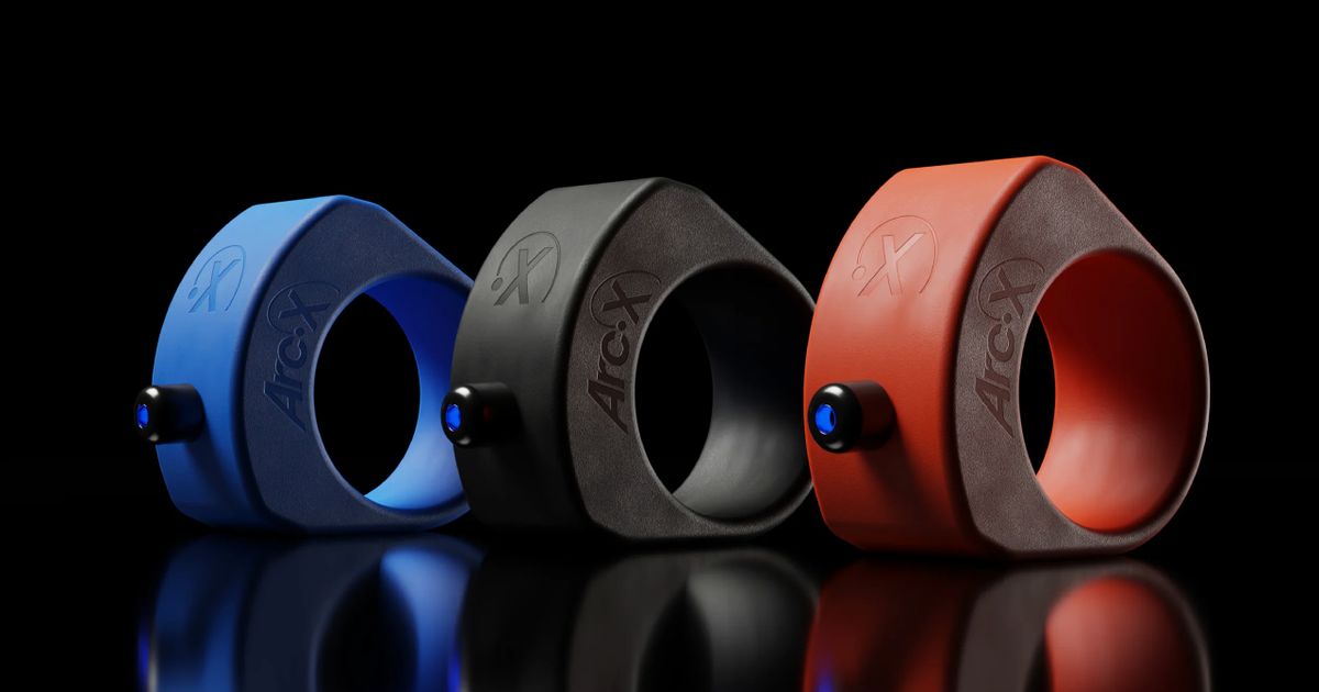 A blue smart ring next to a black one and a red one, all of which featuring black buttons on the top.