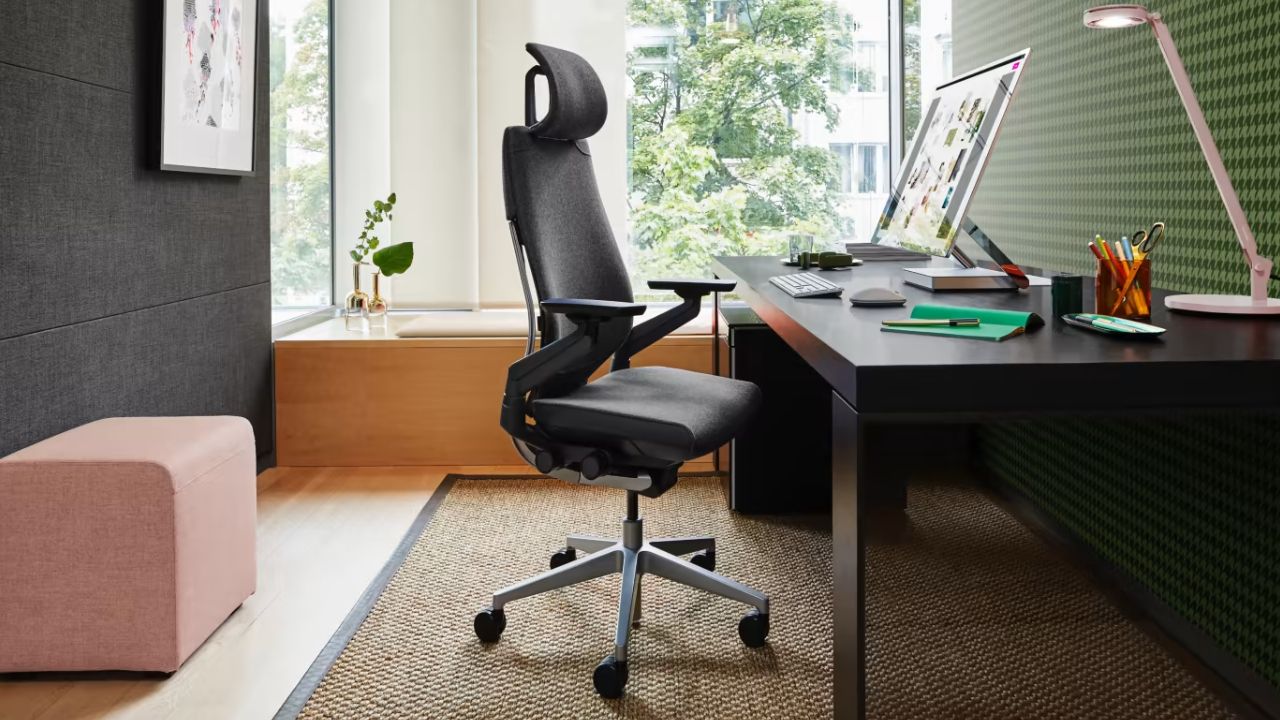 A black office chair with a headset pulled out from a desk with a thin monitor in front of it.