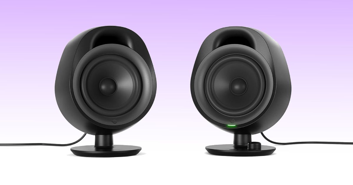 A pair of compact black wired desktop speakers in front of a white and purple gradient background.