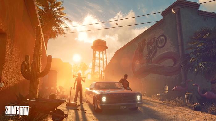 Two people stand next to a stationary car on a dusty side road. The sun is setting. On the wall of the building next to them is a mural of a giant snake trying to eat a biker - Saints Row crossplay