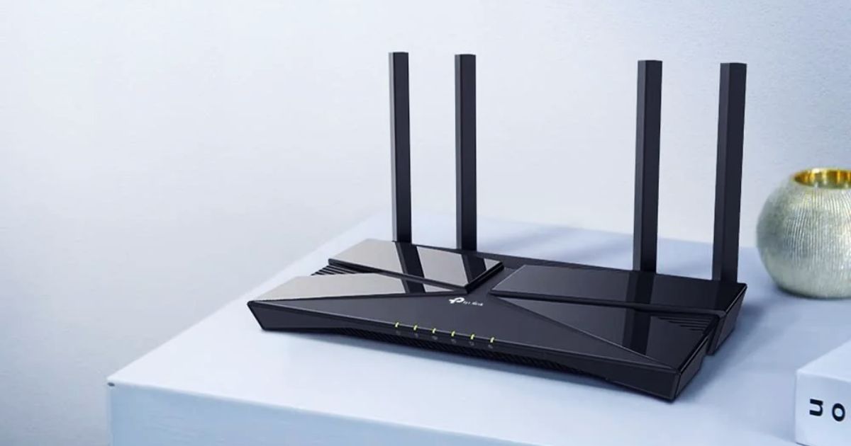 A black WiFi router with four antennae sat on a white table top next to a vase.