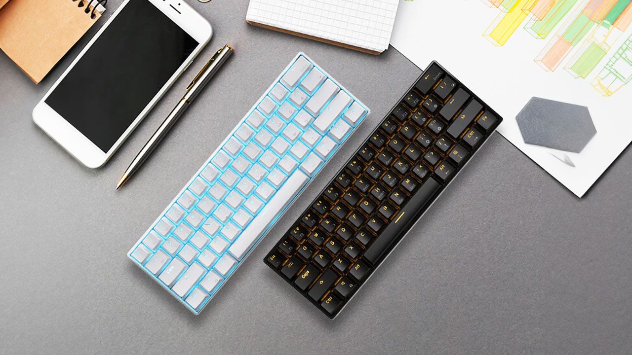 White and black keyboards with backlit keys parallel to one another on a grey desk and sat next to a white iPhone.