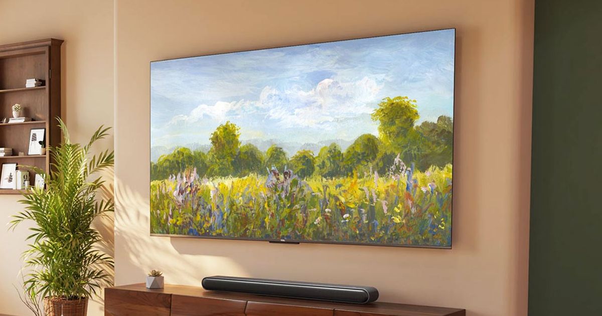 A frameless TV with a painted field and sky setting on the display mounted to a tan wall above a black soundbar and brown cabinet.