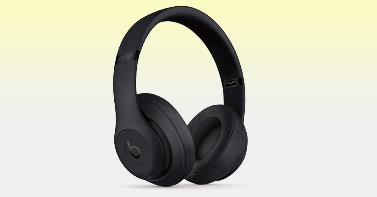 An all-black set of over-ear Beats headphones in front of a white and light yellow gradient background.