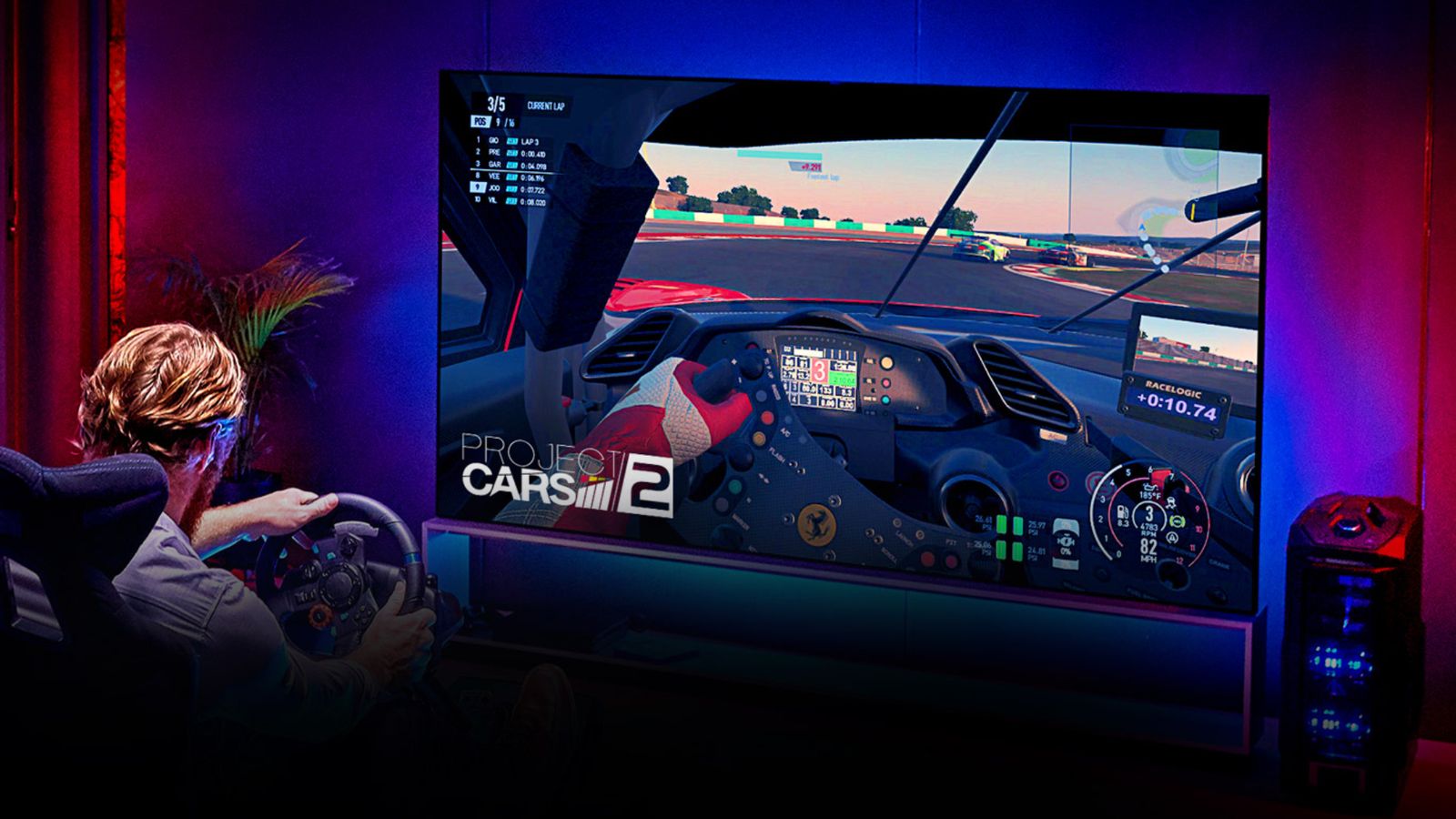 Image of someone playing Project Cars 2 with a racing wheel on a large flatscreen TV with blue and red lighting behind it.