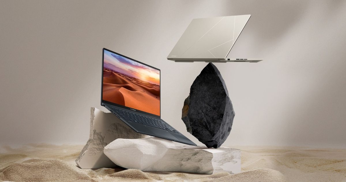 A black laptop with an image orange dunes on the display sat on top of a cream rock, while next to it sits a black rock with a cream laptop balancing on top of it.