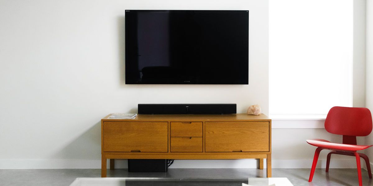 Image of an off TV mounted to a white wall above a brown stand and next to a red chair.