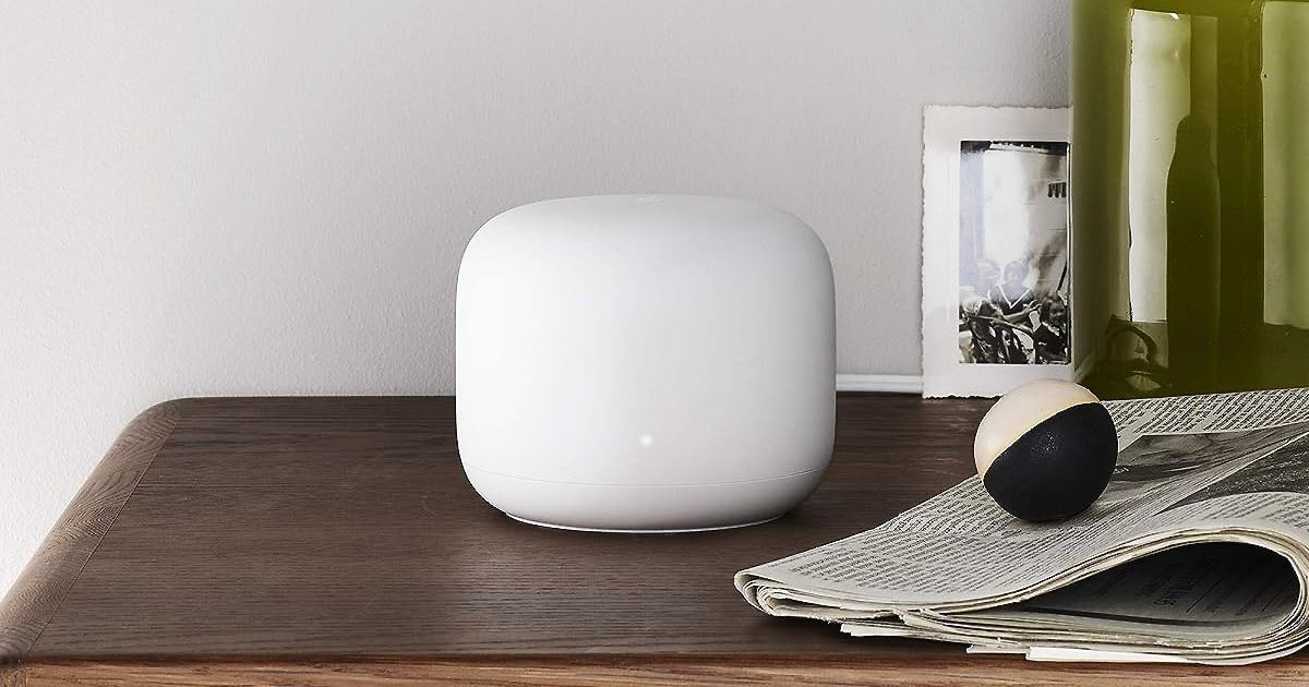 An all-white circular WiFi router sat on a wooden cabinet next to a newspaper.