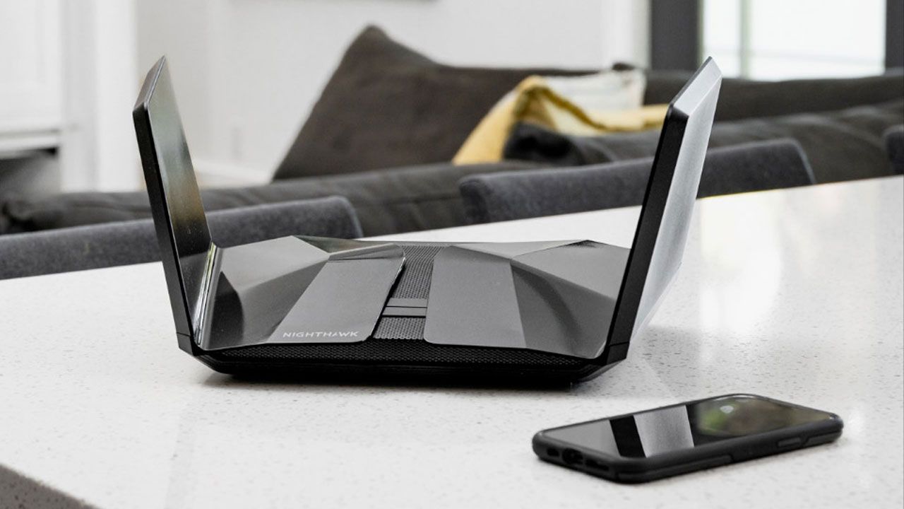 A black Wi-Fi router with two wing-shaped antenna either side sat on a white table next to a black smartphone.