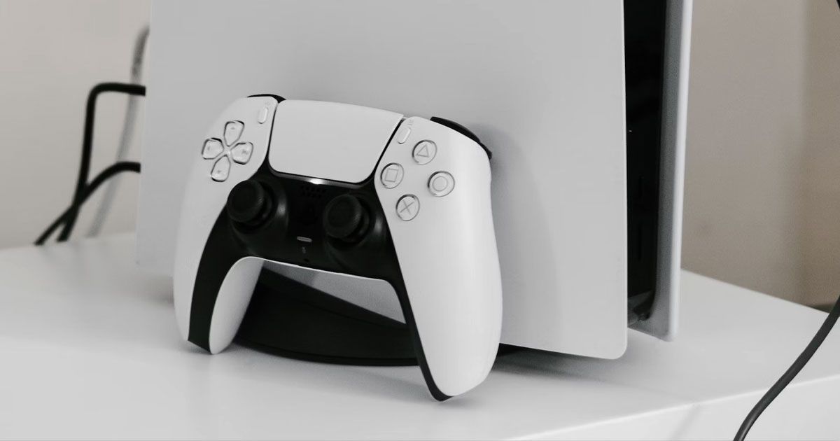 A white and black PS5 controller leaning against a PS5.