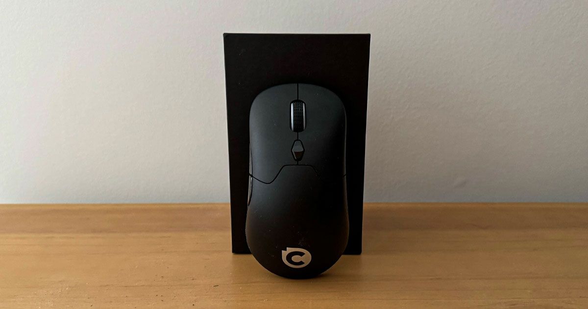 A black wireless mouse leaning against a black box while sat on a brown wood cabinet.