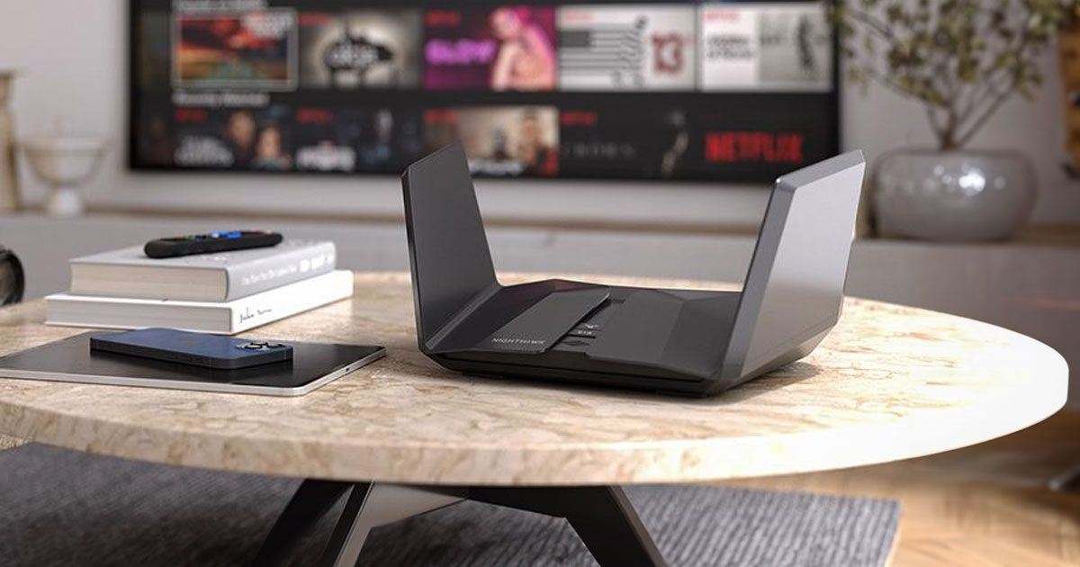 A black, winged router sat on a cream table next to a phone, tablet, and some books.
