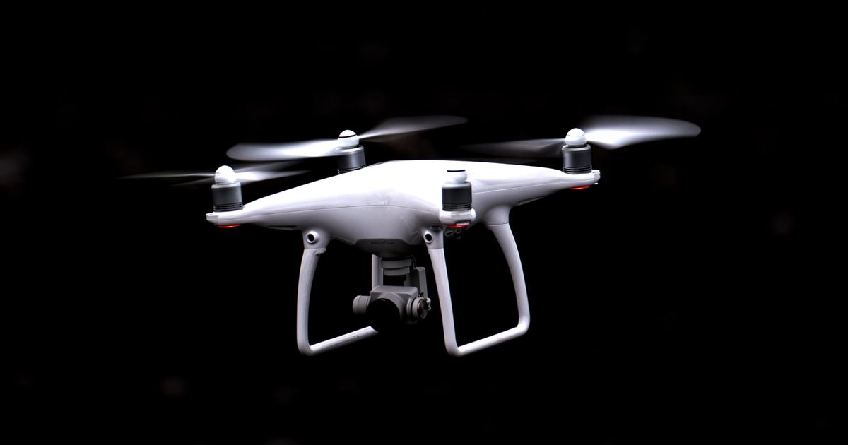 An all-white drone with a camera underneath flying in a black room.
