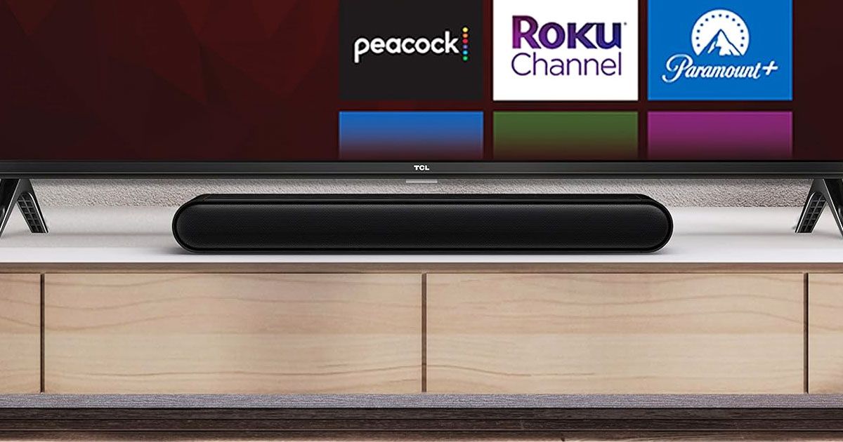 A black rectangular soundbar with curved ends on top of a TV stand and below a black TV.