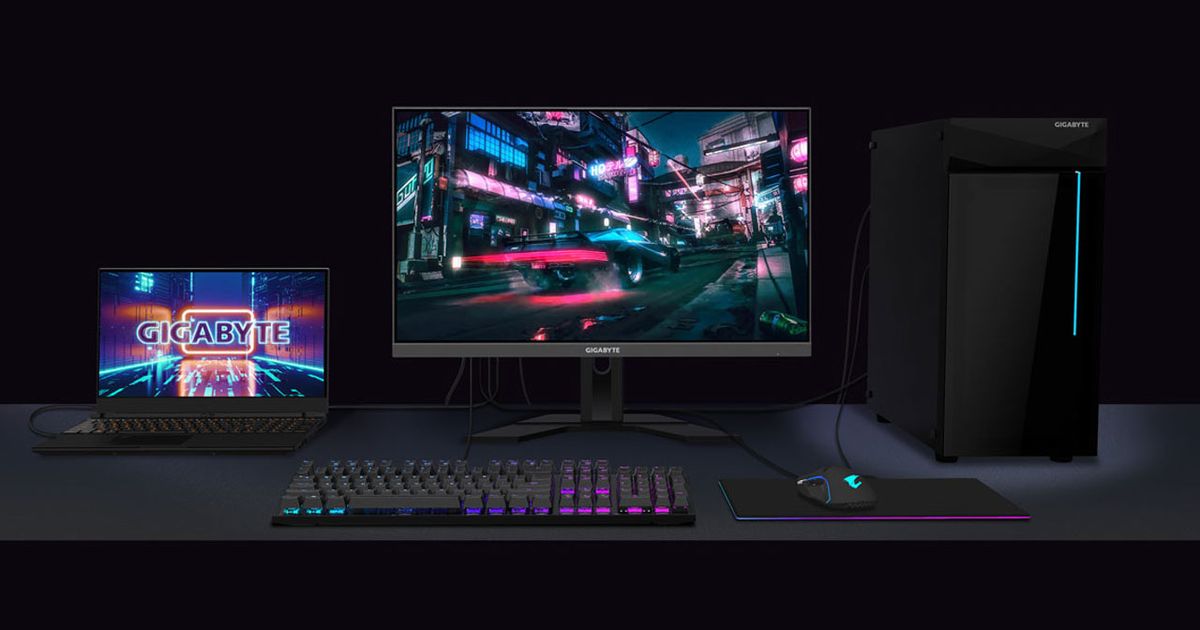 A black monitor with a car speeding through a city on the display next to a Gigabyte laptop, backlit keyboard, mouse, and PC.