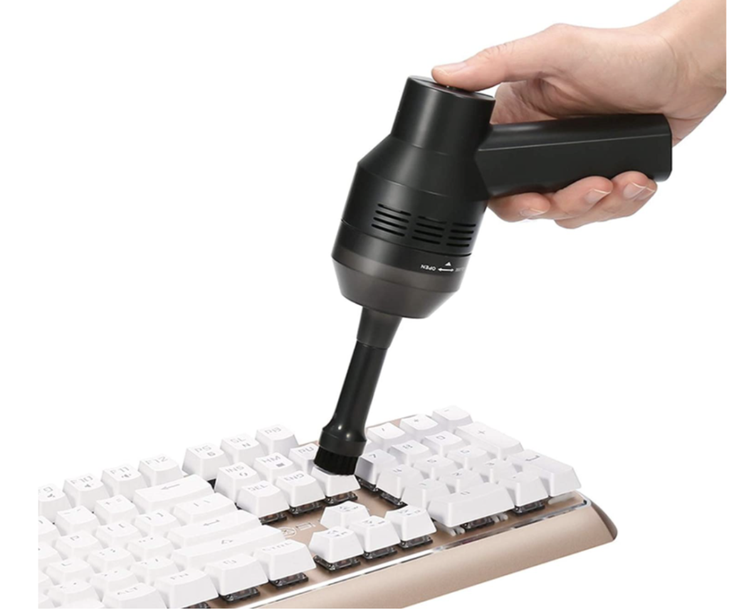 MECO Rechargeable Mini Keyboard Vacuum product image of someone using a black mini vacuum to clean a white keyboard.
