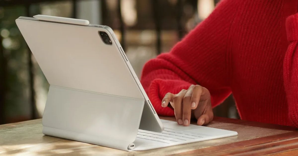 Someone in a red jumper using a white tablet connected to a foldable keyboard.