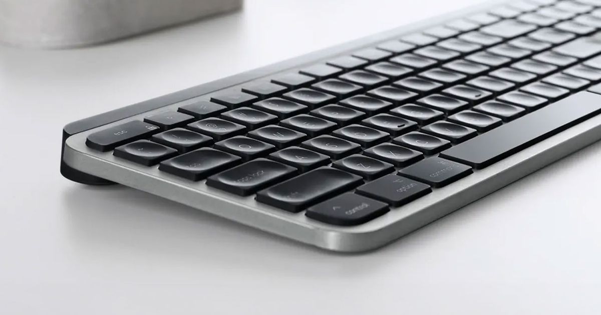 A light grey wireless keyboard on a white desk featuring black keys.
