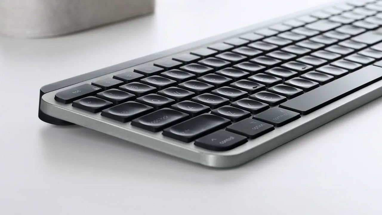 A light grey wireless keyboard on a white desk featuring black keys.