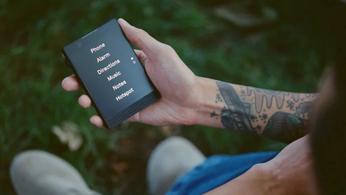 A person with a tattoo on their arm holding the new Light Phone 3 in their hand, with the main menu on-screen