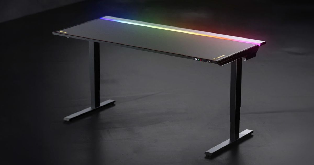 A black gaming desk in a dark room with RGB lighting at the back.