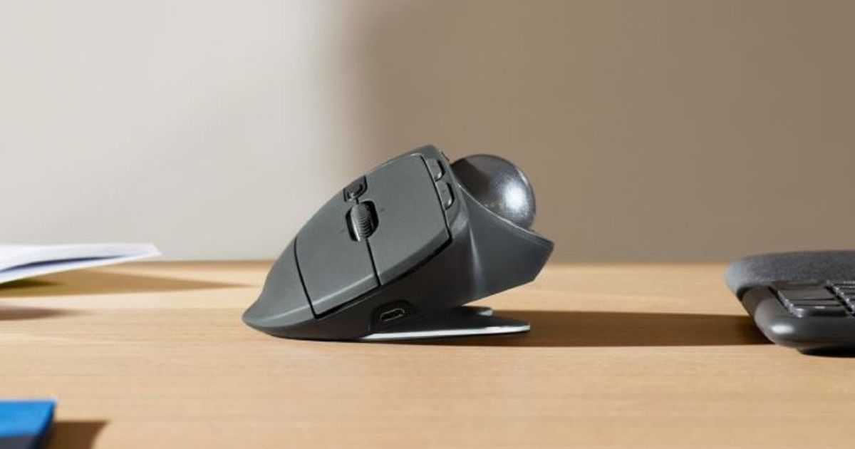 A graphite-coloured ergonomic mouse with a trackball on the left side sat on a light brown desk.