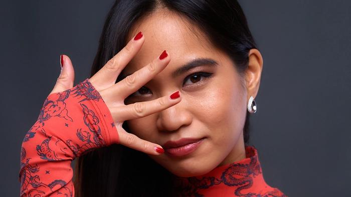 Kayane posing for a portrait covering her face with her fingers on a grey background