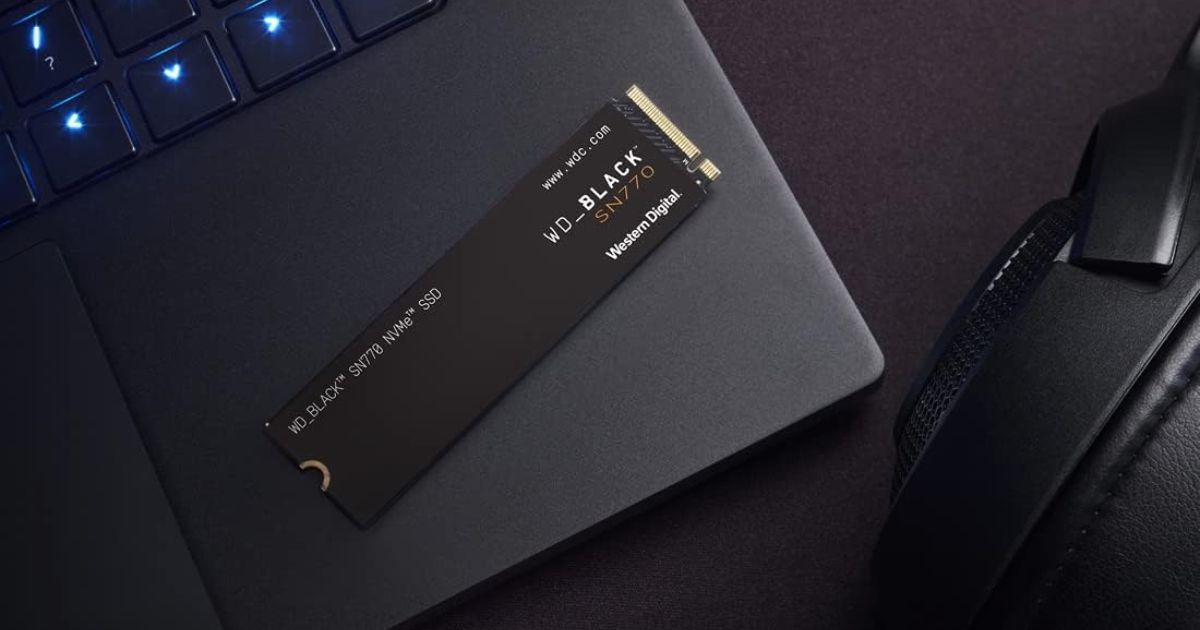 A small, black, rectangular SSD laying on top of a laptop next to a black over-ear headset.