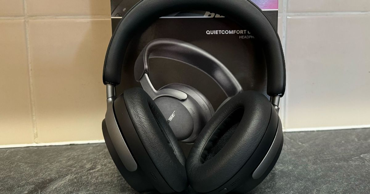 Bose QuietComfort Ultra Headphones in front of the box and a tiled wall