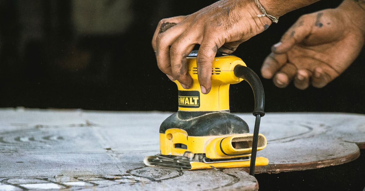 Someone using a yellow and black sander on a sheet of wood.